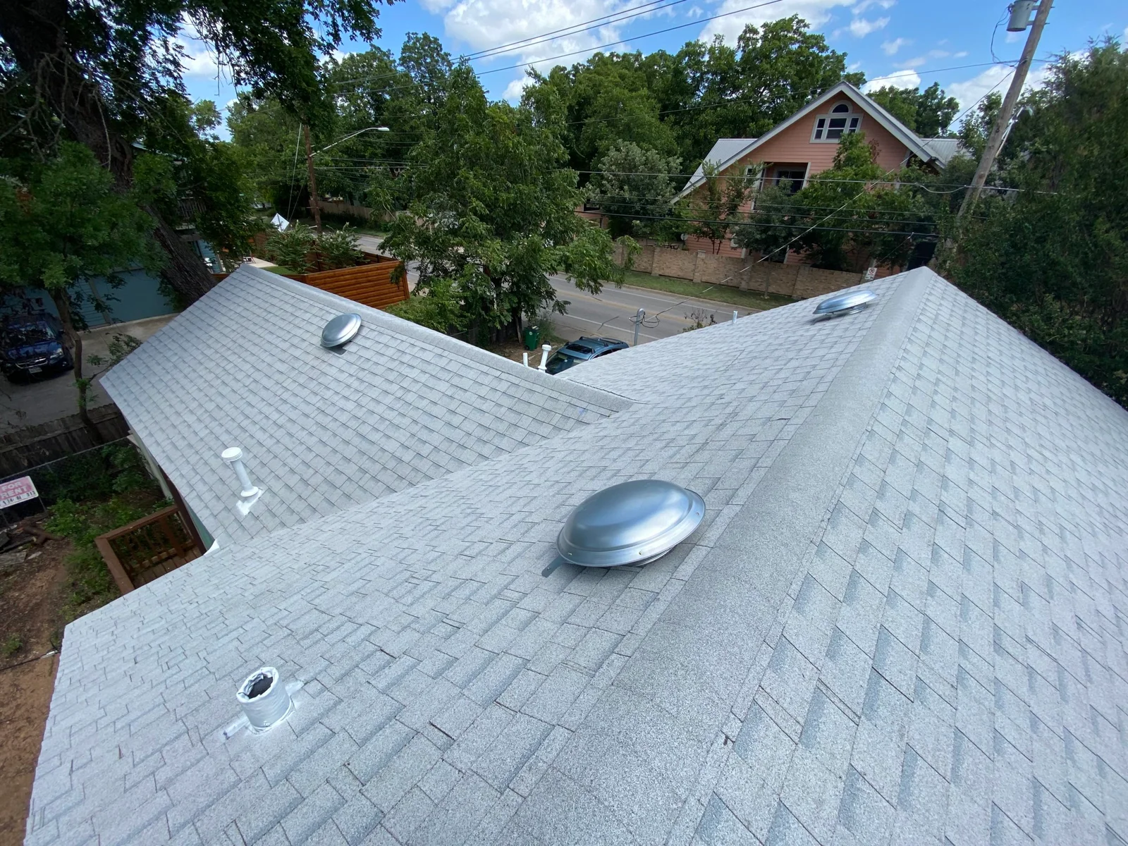 An actual Acura Roofing portfolio photograph showing shingle roofing and roof vents in an Austin neighborhood
